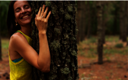 Sportlerin umarmt fröhlich in der Natur einen Baum