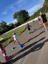 Kinder fahren auf einem Platz mit den Inline Skates durch einen Parkour