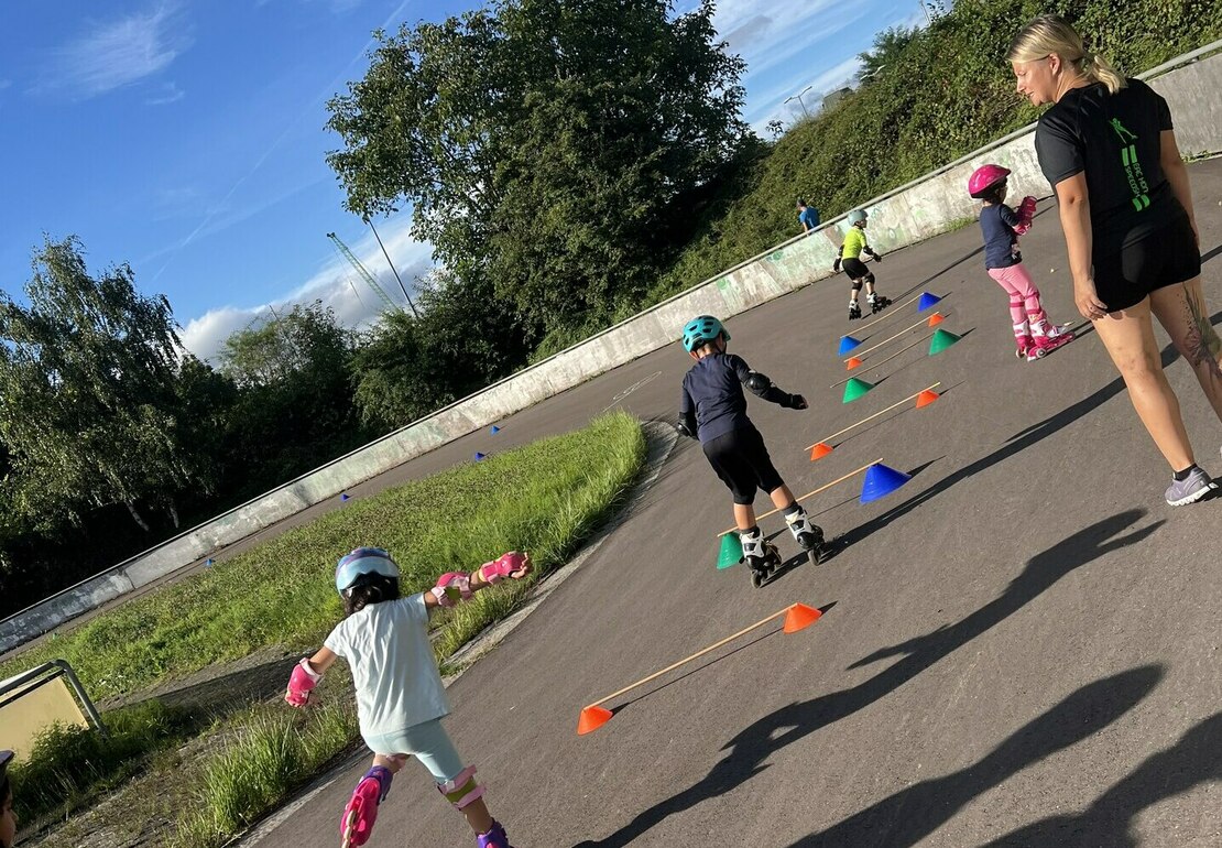 Kinder fahren auf einem Platz mit den Inline Skates durch einen Parkour